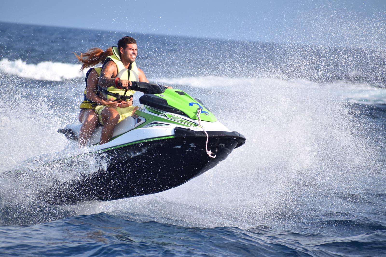Two people riding a jet ski on the ocean, creating splashes.