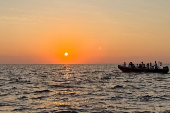 Boat with people on calm sea at sunset.