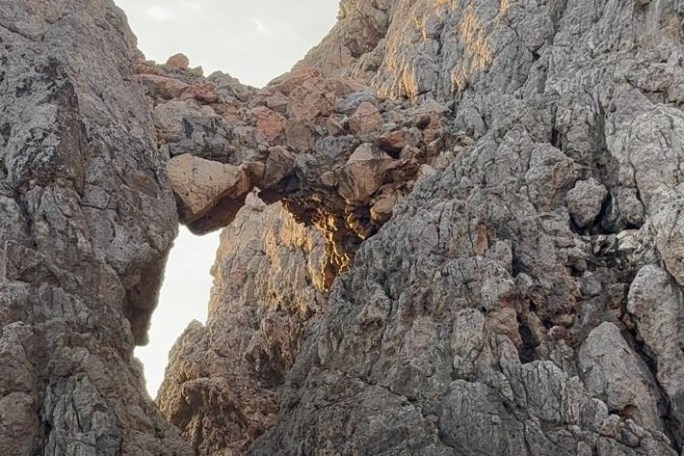 Natural rock arch formation in rugged mountain landscape.