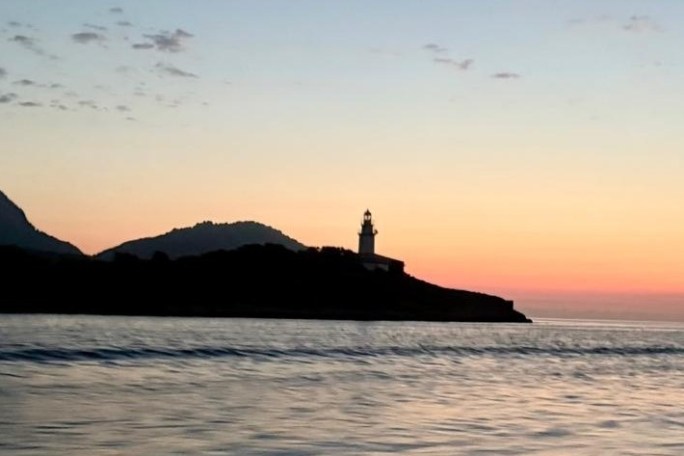 Lighthouse on a coastal hill at sunset, with calm sea waves.