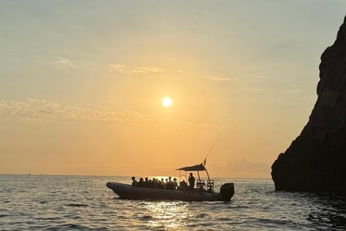 Boat with people at sunset near a rocky cliff.