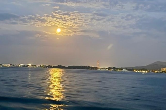 Moonlit coastal scene with distant city lights and calm water.