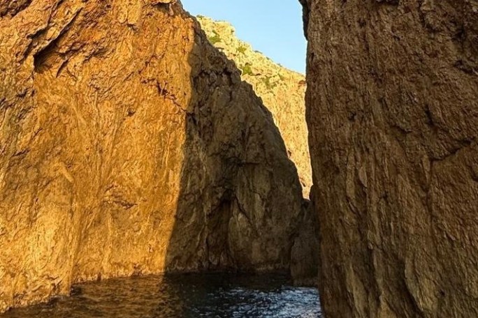 Rocky cliffs illuminated by sunlight with water below.