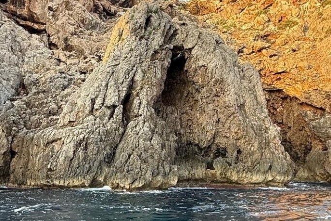 Rocky cliff with a natural arch near the sea.