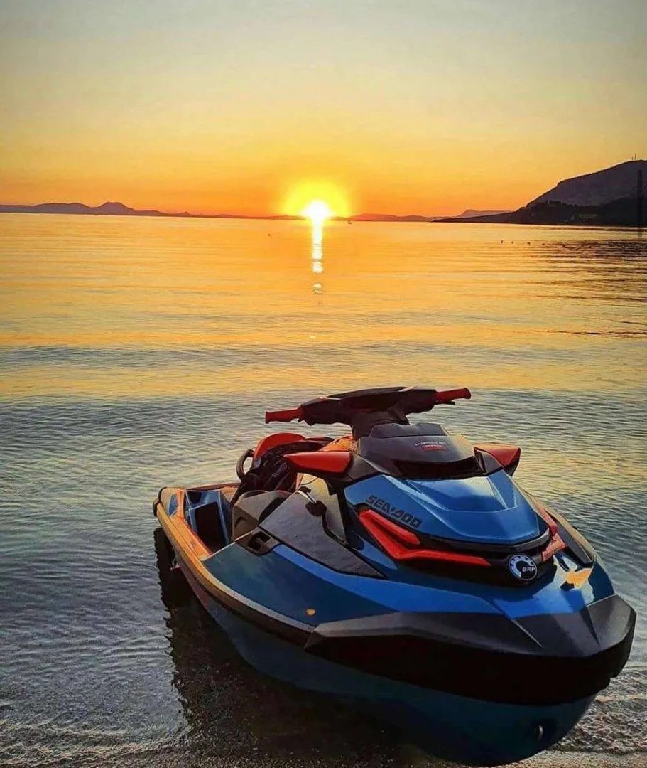 Jet ski on calm sea at sunset with mountains in background.