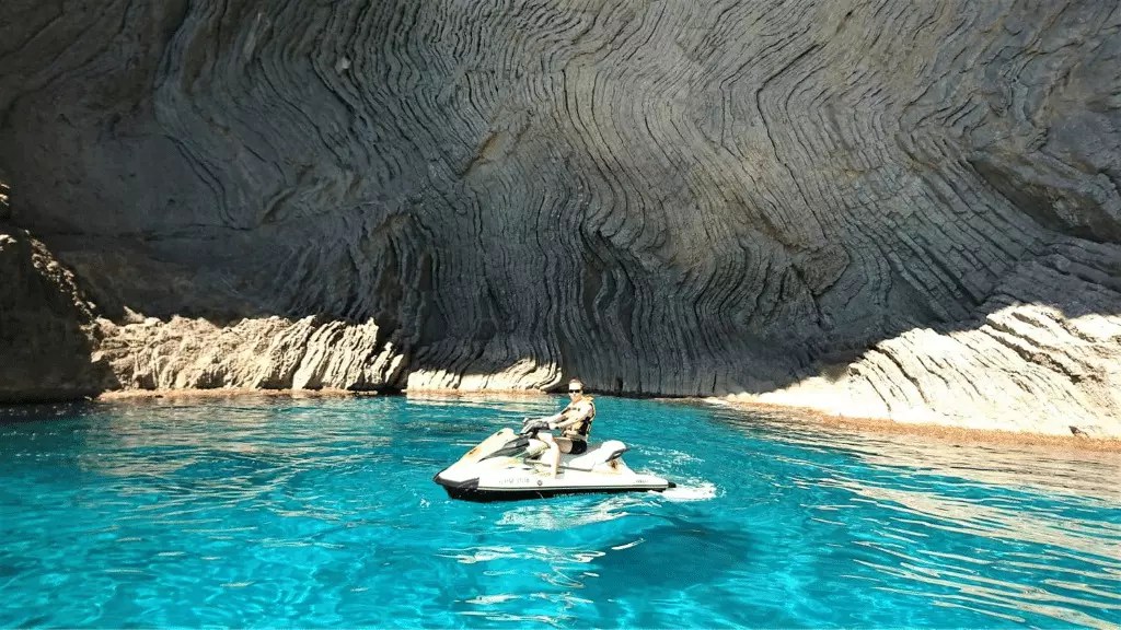 Person on a jet ski in a turquoise water cave with layered rock walls.
