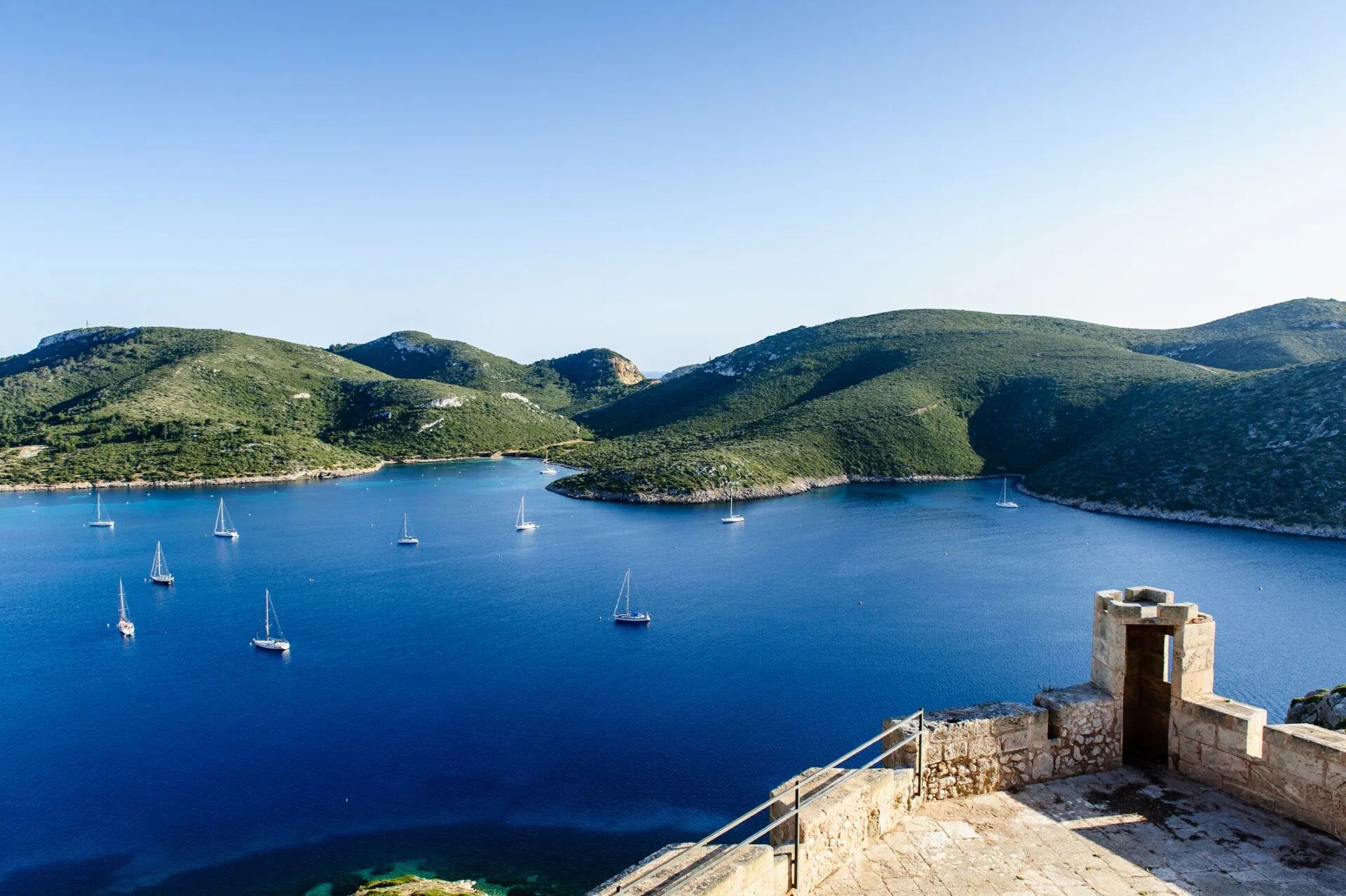 Scenic view of a bay with sailboats and green hills under a clear blue sky.
