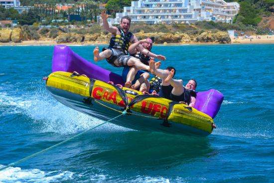 Group riding an inflatable banana boat on the ocean, with visible excitement and splashing waves.
