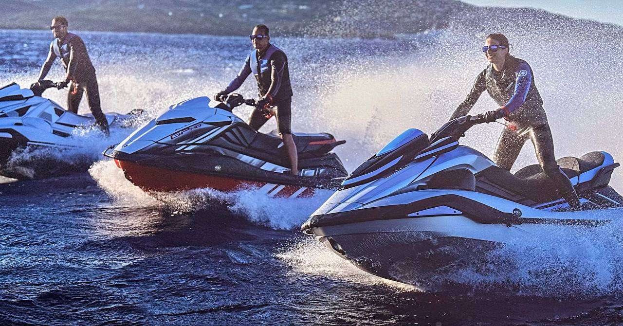 Three people riding jet skis on a sunny day with splashing water.