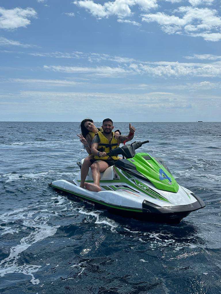 Two people on a green and white jet ski in the ocean, wearing yellow life jackets.