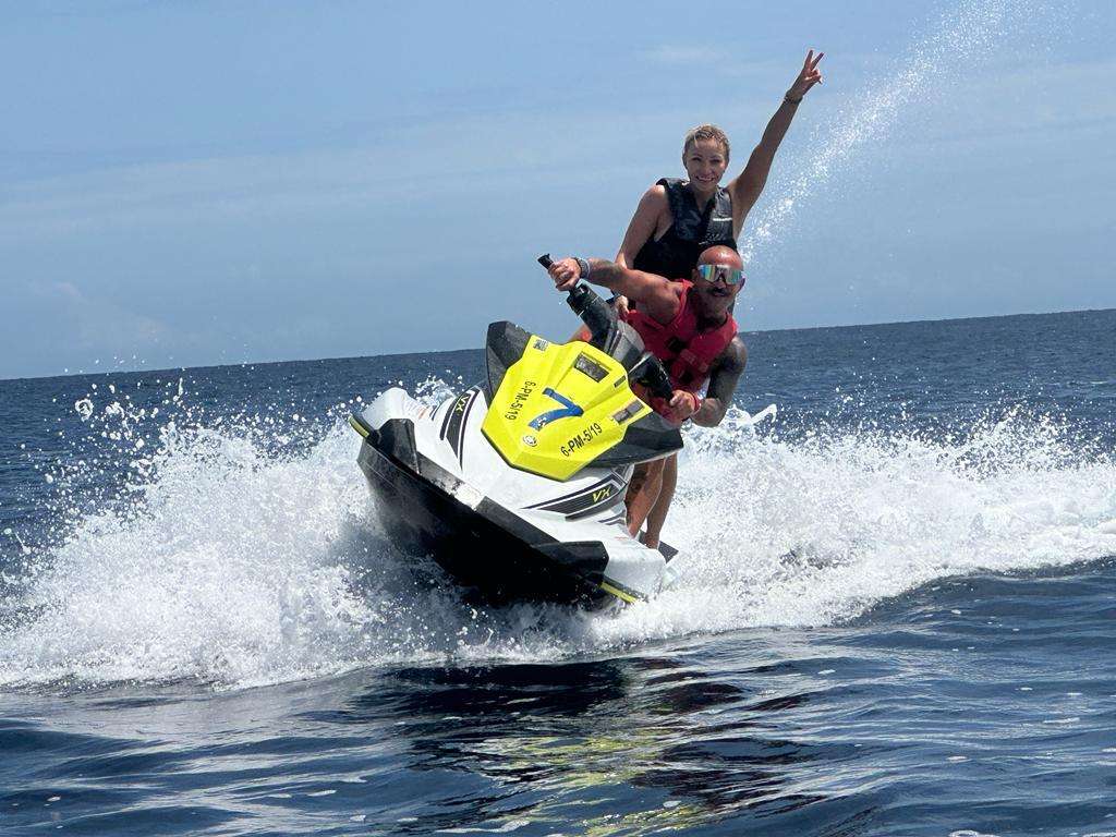 Two people on a jet ski, one raising an arm, riding on ocean waves.