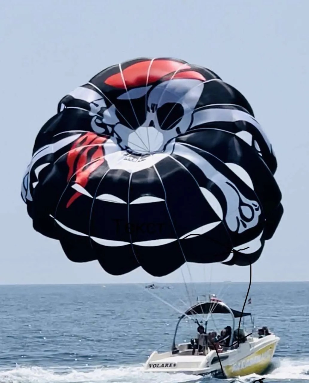Boat towing a large parachute with a skull design over the ocean.