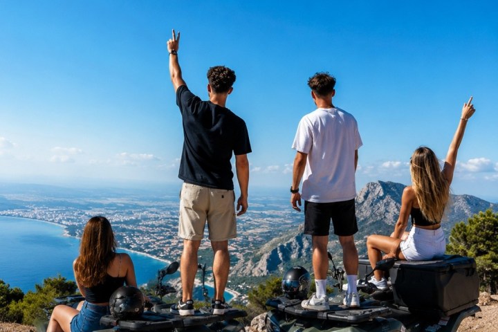 Four people on ATVs posing with peace signs on a mountain with ocean view.