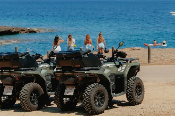 Two ATVs parked on sandy beach with people and ocean in background.