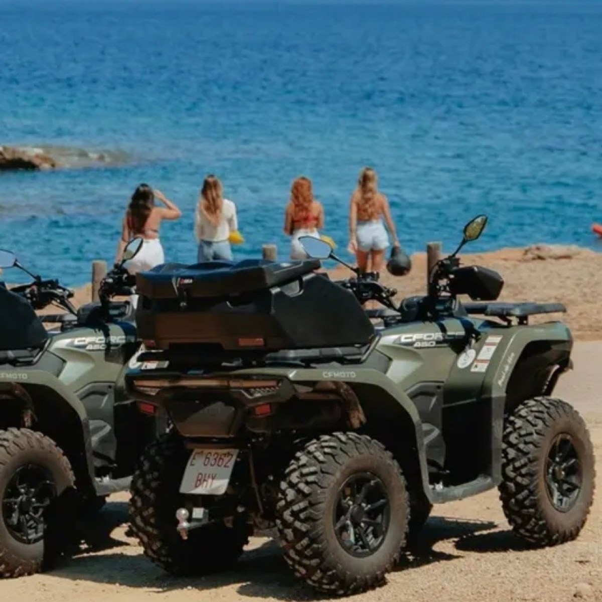 Two ATVs on a sandy beach with people and ocean in the background.